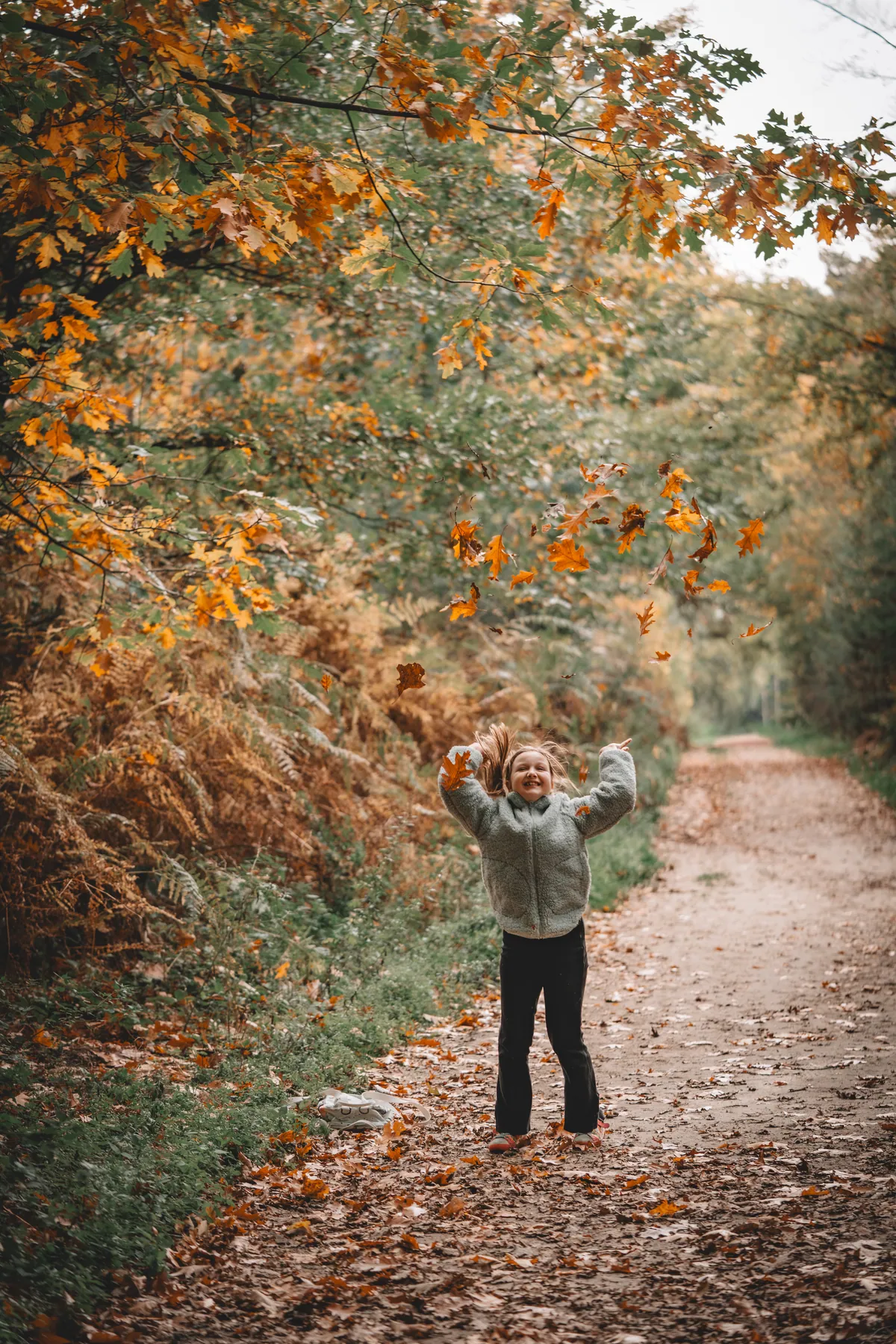 Mädchen wirft auf einem herbstlichen Waldweg Laub in die Luft