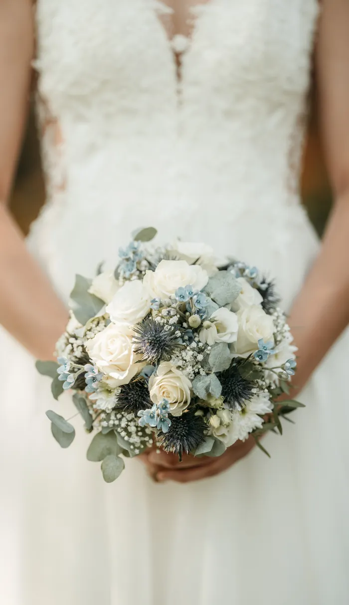 Brautstrauß mit weißen Rosen und blauen Disteln vor dem Brautkleid